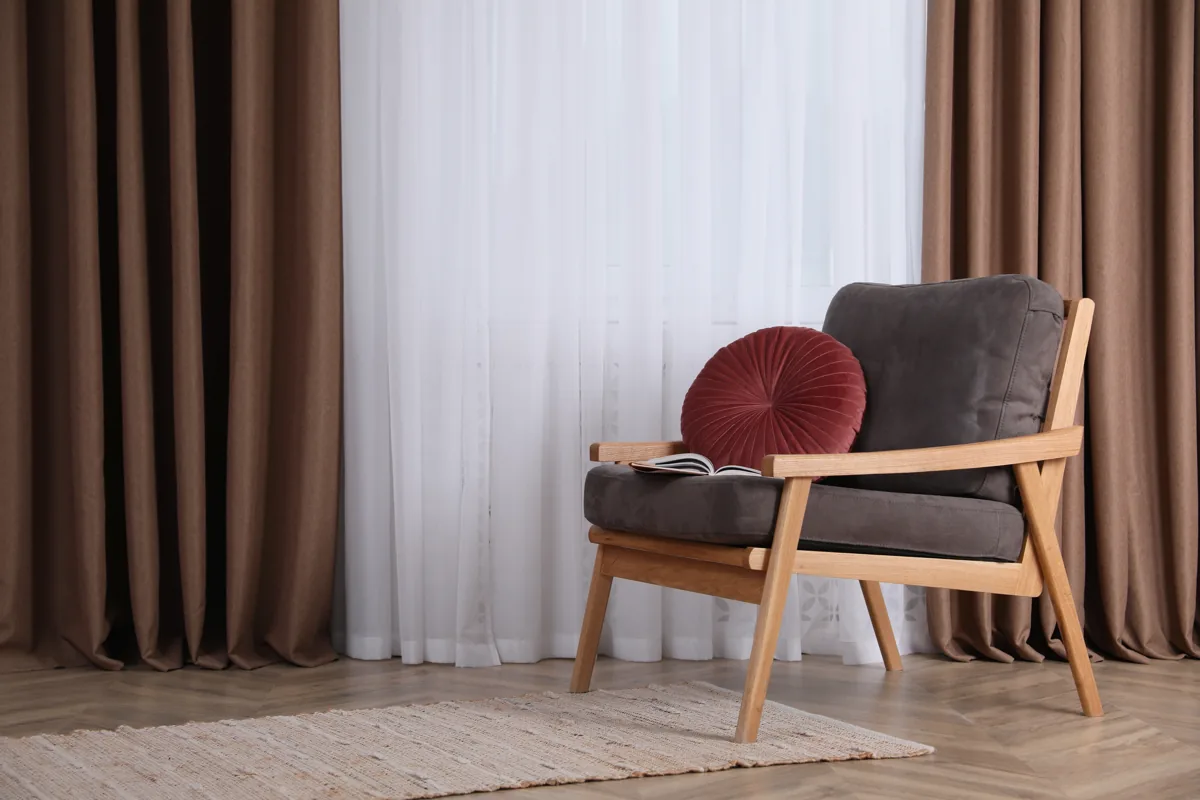 Floor-length taupe drapes and a sheer curtain beside a contemporary armchair