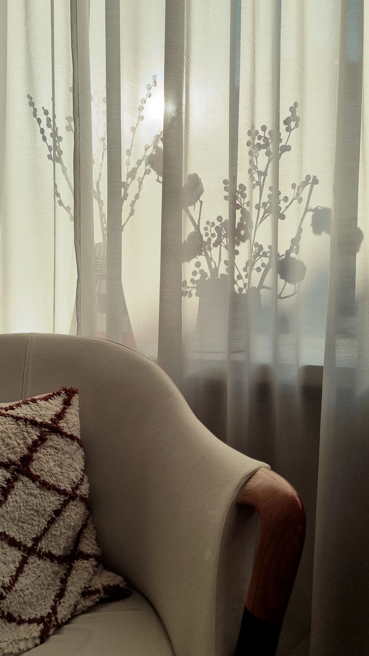 Sunlight passing through sheer curtains beside an upholstered chair
