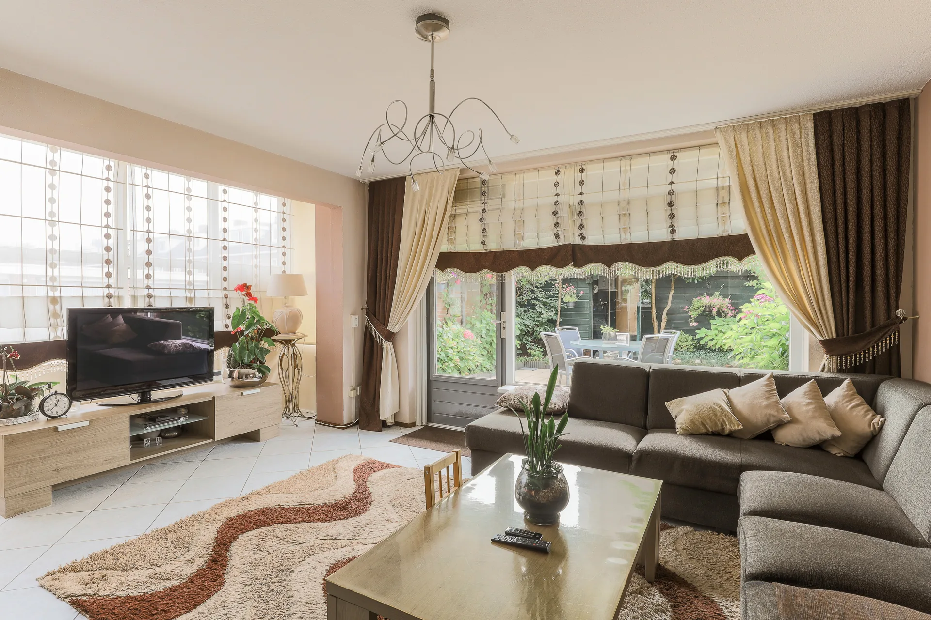 A neutral living room with floor-to-ceiling drapes, natural light and a curved rug
