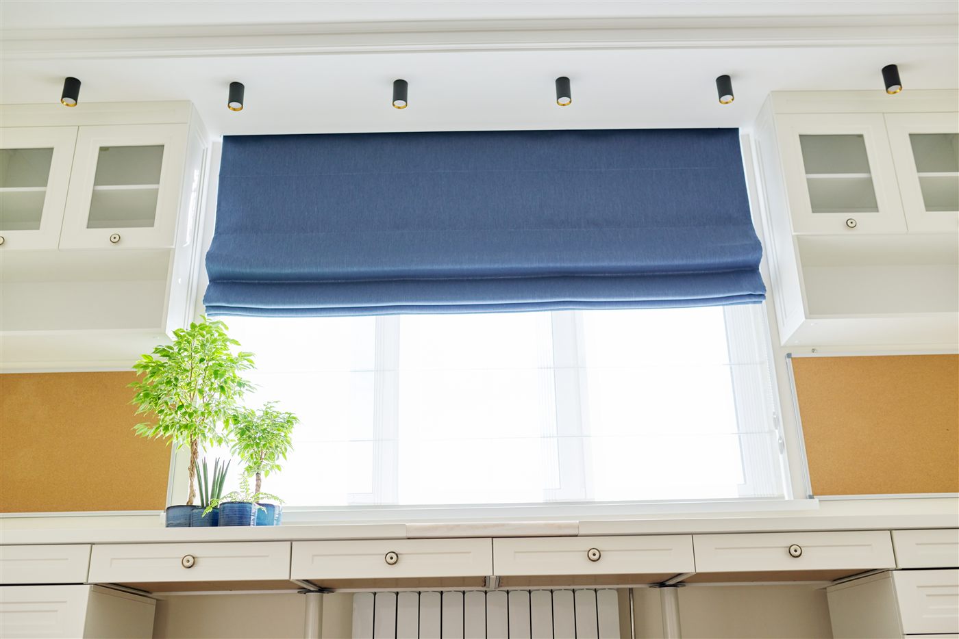 Blue Roman shade above a bright window with white built-in cabinets