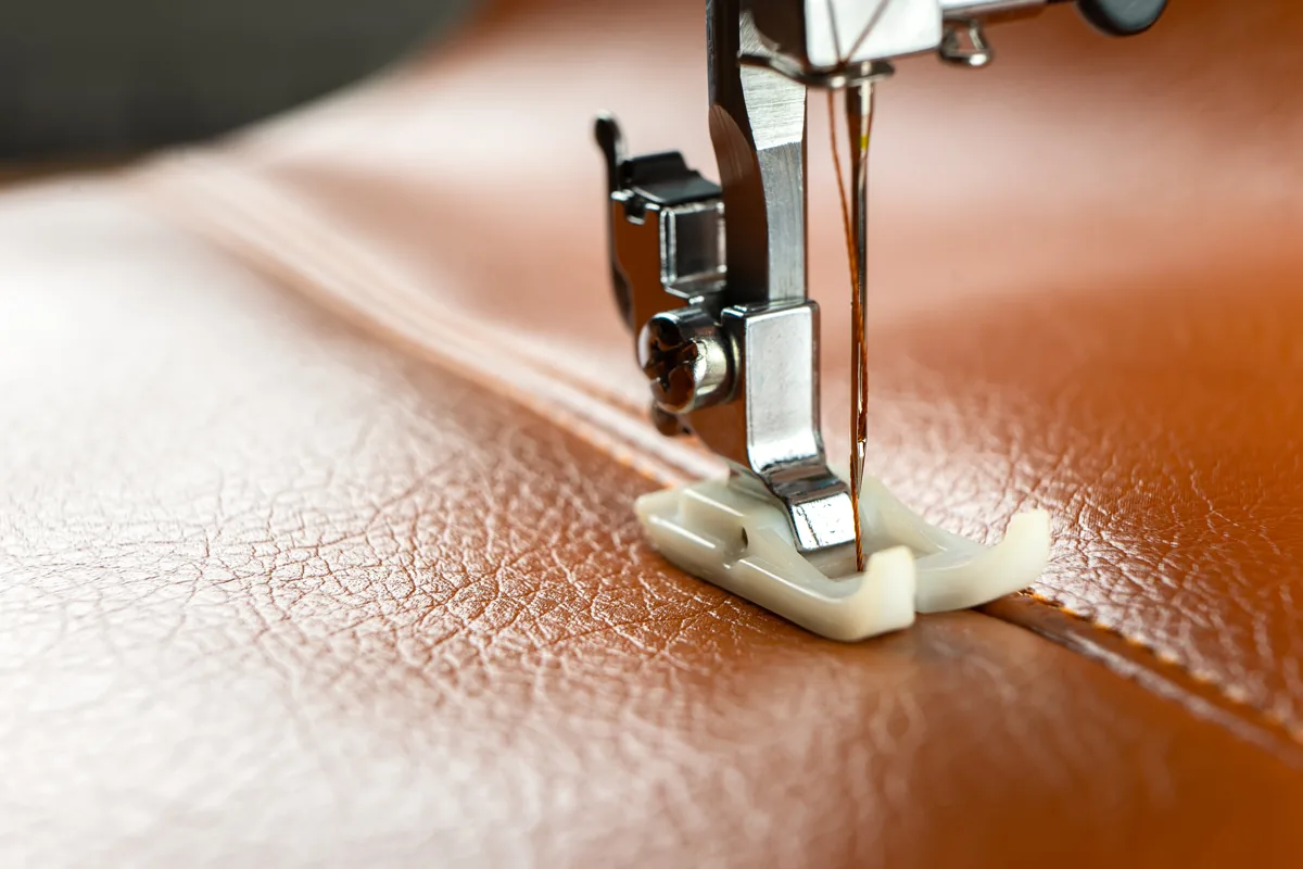 A sewing machine carefully stitching warm brown leather