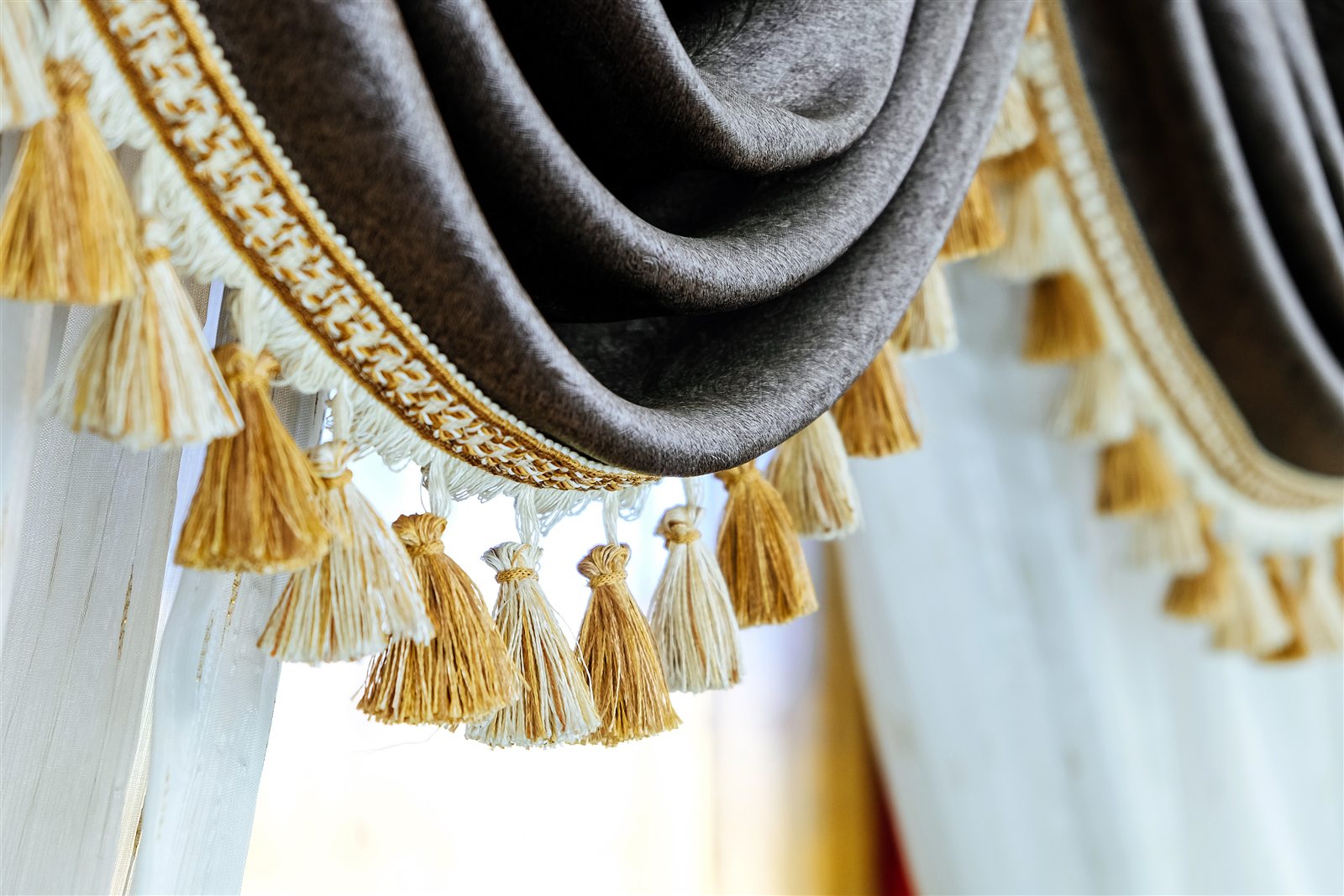 Close-up of a brown draped valance finished with cream and gold tassels